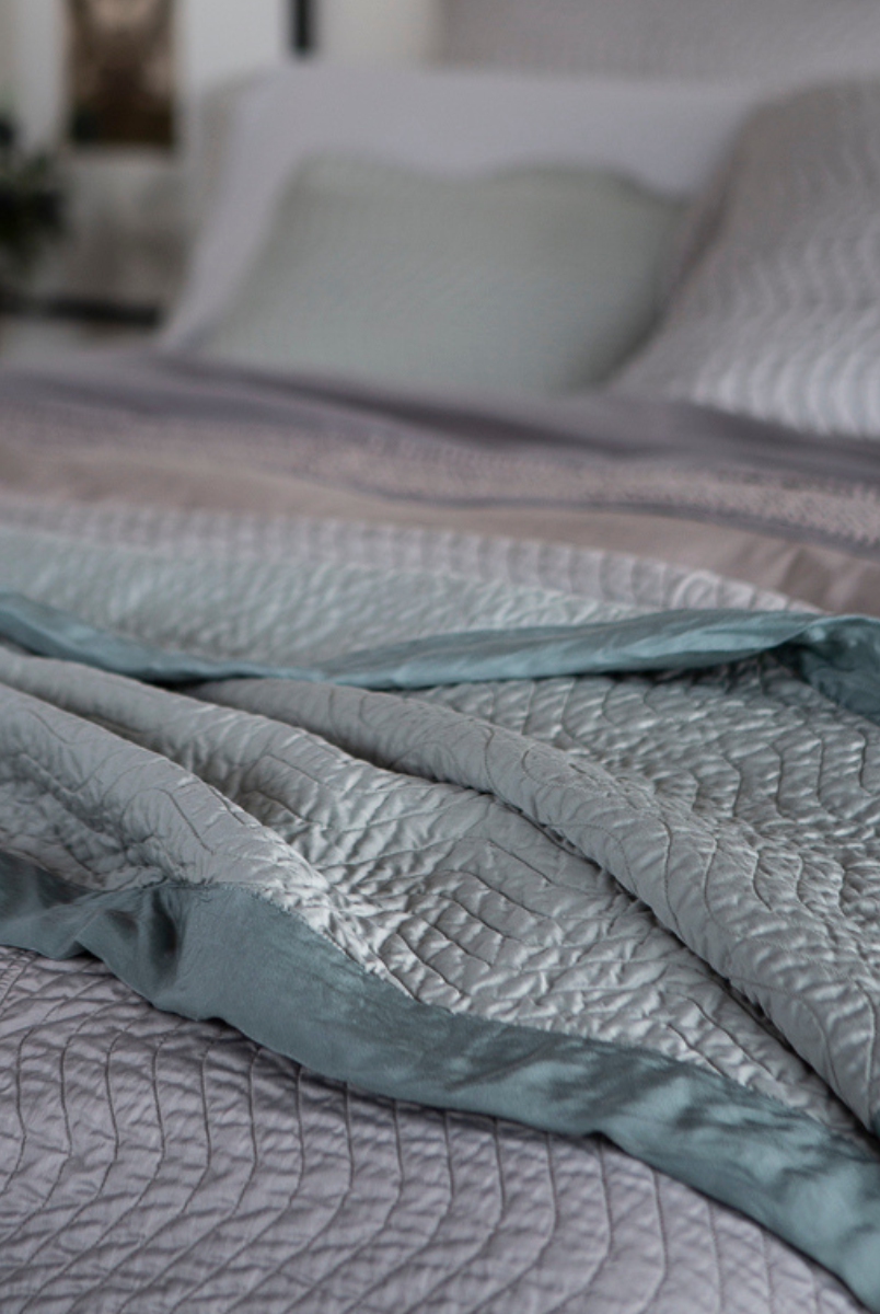[allvariants]: a close up of a quilted cotton sateen throw blanket rumpled and layered at the foot of a bed.