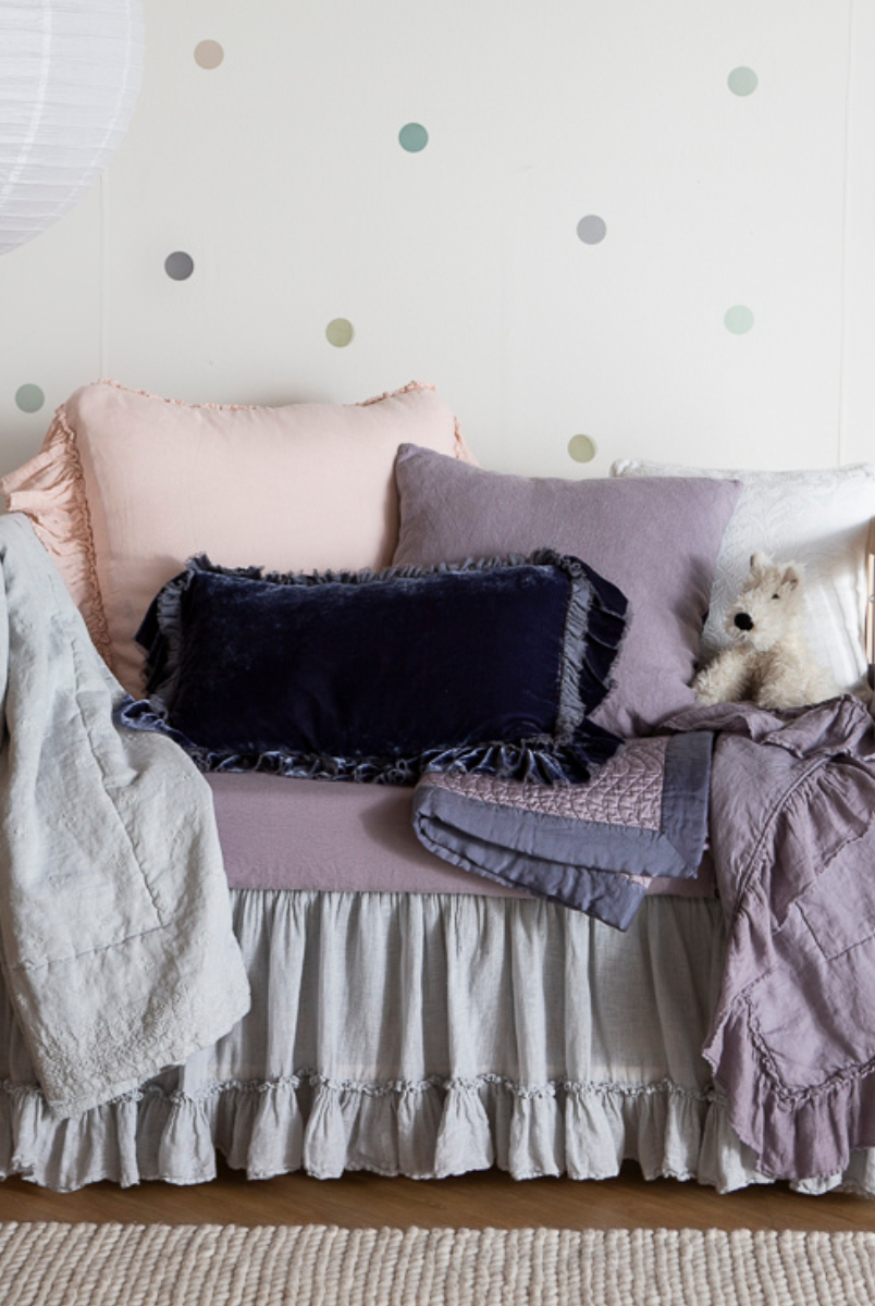 [allvariants]: a feminine crib dressed in french lavender, pearl and cloud with several throw pillows and a few baby blankets.