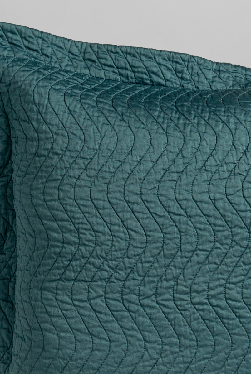 Cenote: a close up of a pillow corner showing the flange framing quilted cotton sateen shot against a white background. 