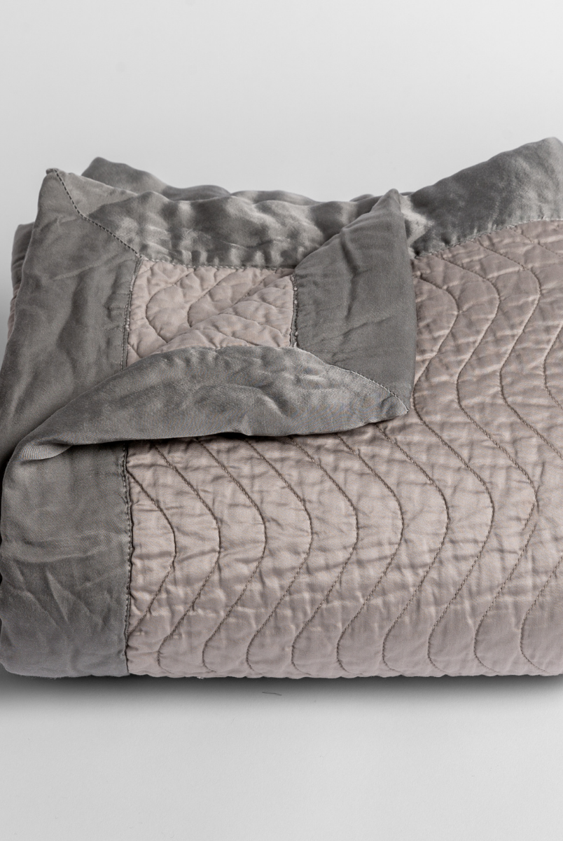 Fog: a folded quilted cotton sateen baby blanket with its corner folded down to show the trim contrast - shot against a white background. 