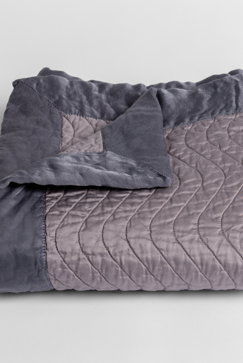 French Lavender: a folded quilted cotton sateen baby blanket with its corner folded down to show the trim contrast - shot against a white background. 