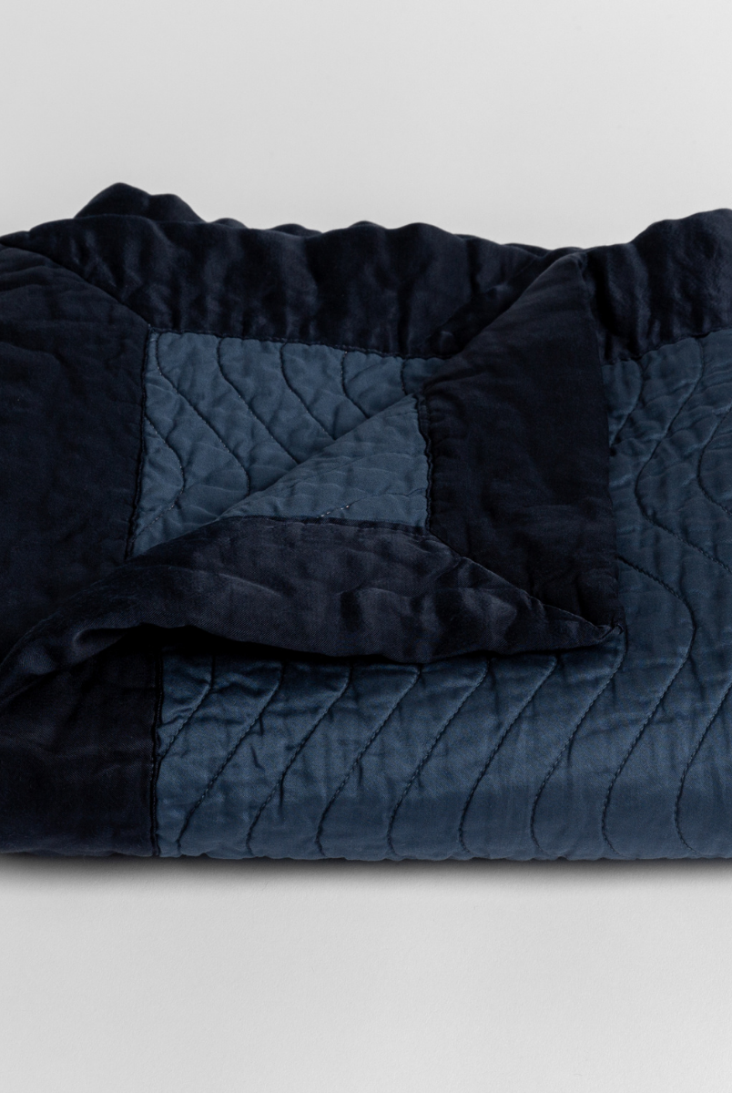 Midnight: a folded quilted cotton sateen baby blanket with its corner folded down to show the trim contrast - shot against a white background. 