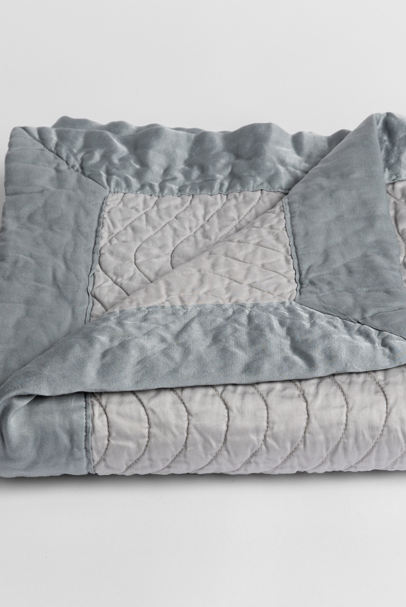 Mineral: a folded quilted cotton sateen baby blanket with its corner folded down to show the trim contrast - shot against a white background. 