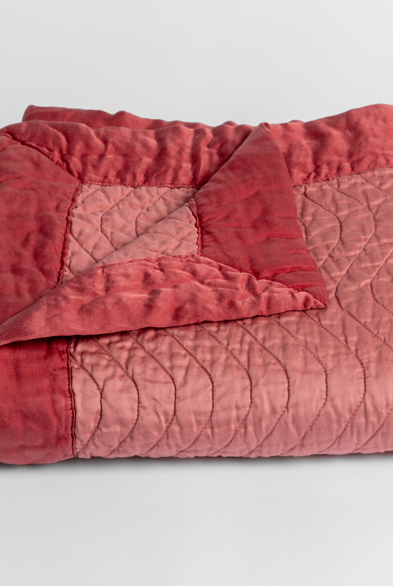 Poppy: a folded quilted cotton sateen baby blanket with its corner folded down to show the trim contrast - shot against a white background. 