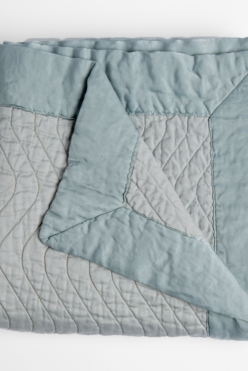 Cloud: a folded quilted cotton sateen throw blanket with its corner folded down to show the trim contrast - shot against a white background. 