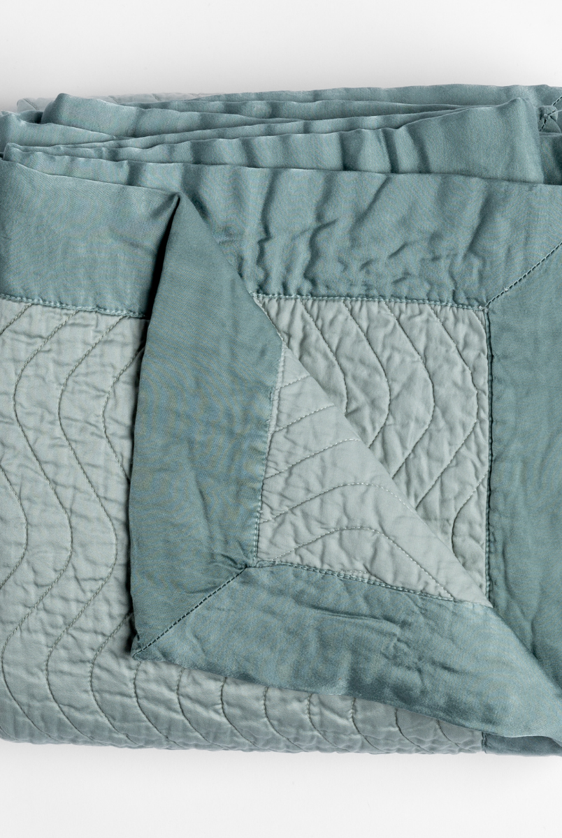 Eucalyptus: a folded quilted cotton sateen throw blanket with its corner folded down to show the trim contrast - shot against a white background. 