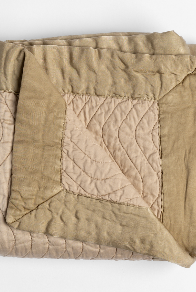 Honeycomb: a folded quilted cotton sateen throw blanket with its corner folded down to show the trim contrast - shot against a white background. 