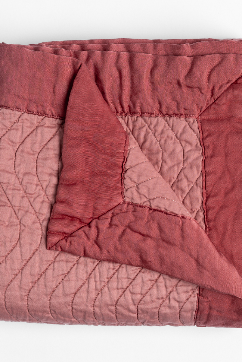 Poppy: a folded quilted cotton sateen throw blanket with its corner folded down to show the trim contrast - shot against a white background. 
