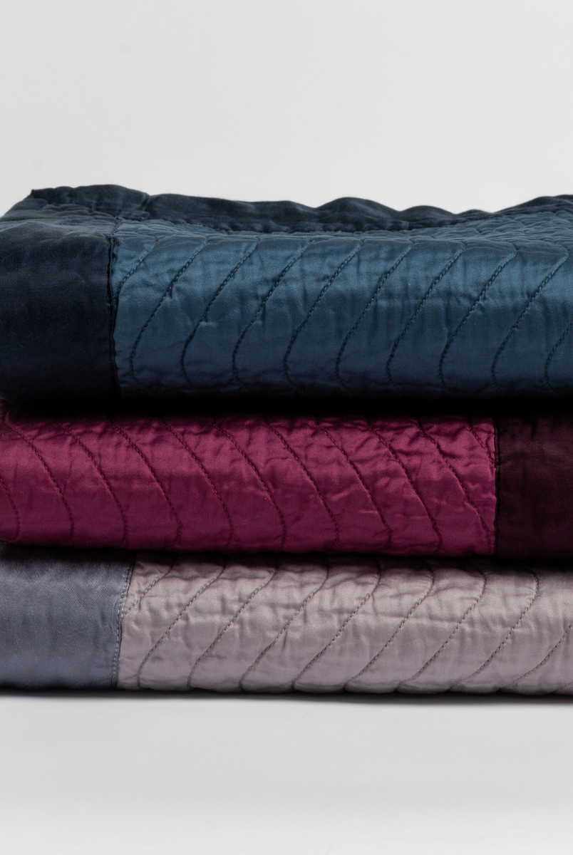 [allvariants]: a stack of three quilted cotton sateen throw blankets in midnight, fig and french lavender.