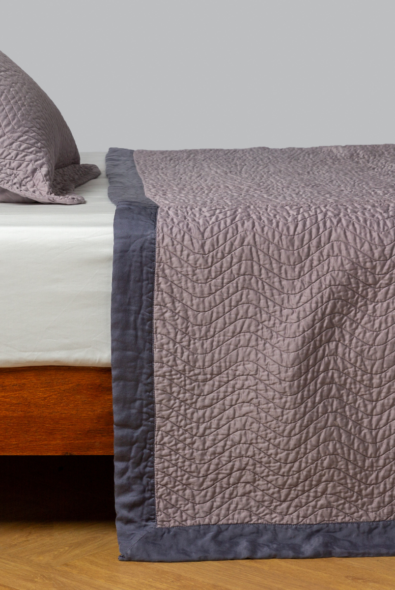 French Lavender: quilted cotton sateen coverlet with matching sham on a winter white fitted sheet - side view. 