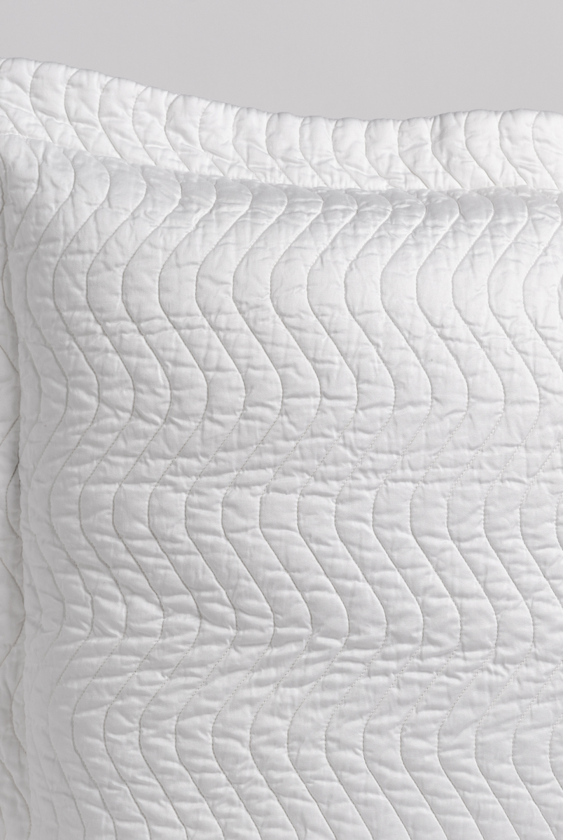 White: a close up of a pillow corner showing the flange framing quilted cotton sateen shot against a white background. 
